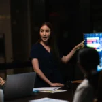 A professional woman presents data on a screen to colleagues in a conference room.