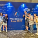 Members of the Web Development Team posing in front of a colorful wall covered with greetings in various languages at WordCamp Asia 2025