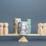 A wooden balance scale with money on one side and small figures representing people on the other side.