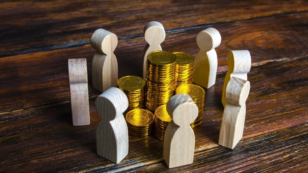 Gold coins scattered among wooden figures on a textured wooden table surface.