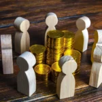 Gold coins scattered among wooden figures on a textured wooden table surface.