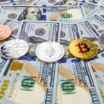 Assorted physical cryptocurrency coins including Bitcoin, Ethereum, Litecoin, and others displayed on top of scattered US $100 bills.