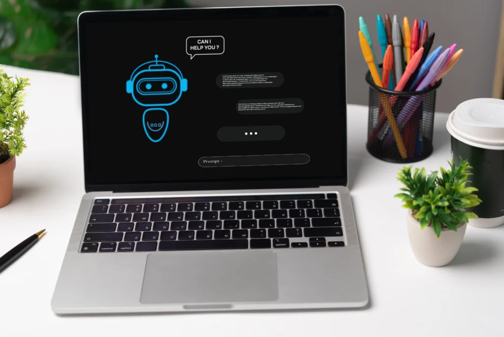 A laptop on a desk shows a chatbot interface on its screen, with a speech bubble saying "Can I help you?" Nearby are colorful pens, a small plant, and a coffee cup, creating a workspace vibe.