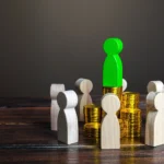 A green figure stands triumphantly atop a large pile of gold coins, symbolizing wealth and success.